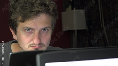 Strange man surfing the web looks at camera and shushes with his finger over his mouth, as if conveying a secret should be kept.
