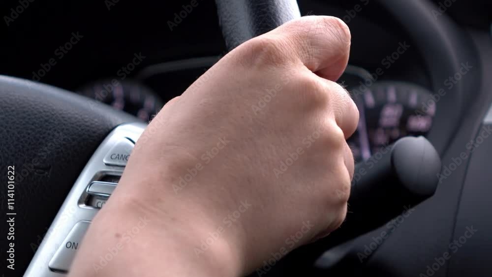 Hand of female gripping wheel while steering the car.
