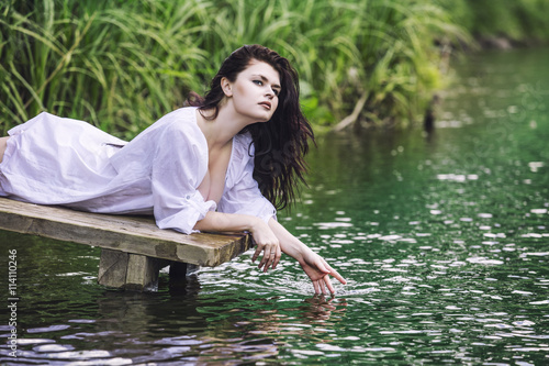 Young beautiful brunette woman enjoys the lake with clear water