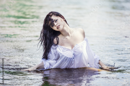 Young beautiful brunette woman enjoys the lake with clear water