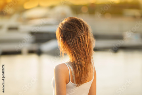 A young girl on the background of boats. Sunset in the Yacht Club. Gorgeous warm bokeh.