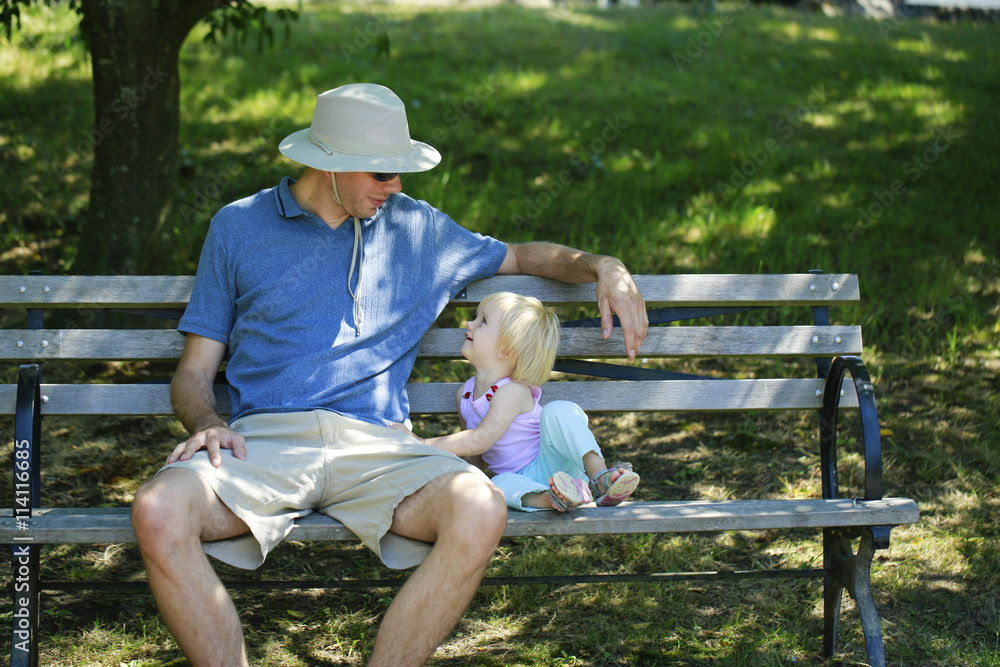 Fototapeta premium Caring father sits with the kid on a wooden bench