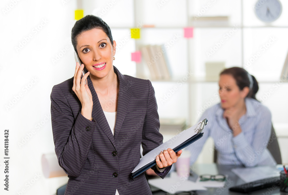Businesswoman sitting at her desk with colleague on background Businesswoman sitting at her desk with colleague on background