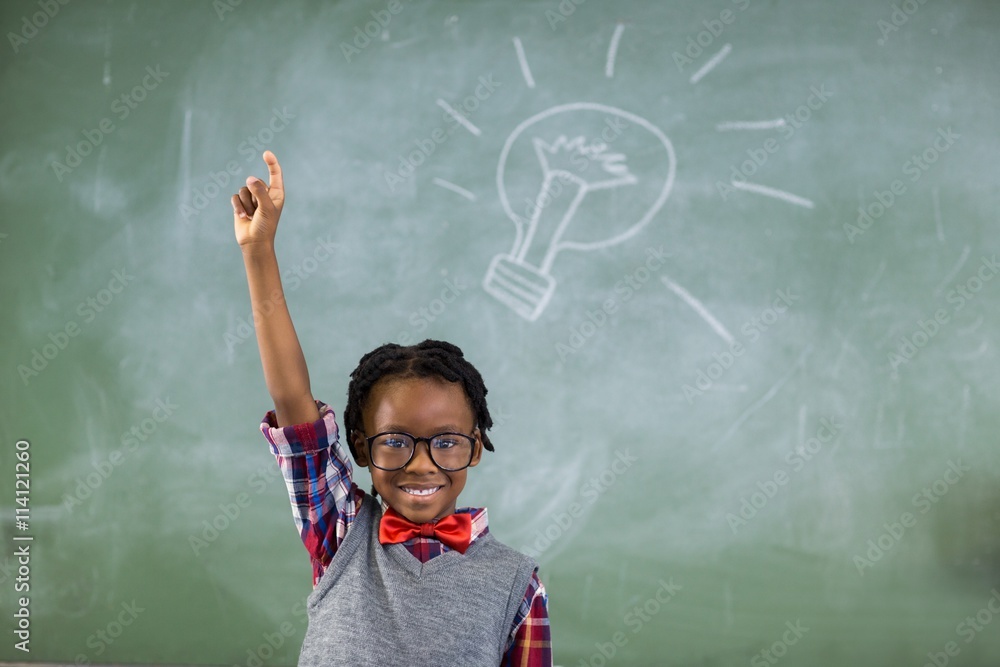 Portrait of schoolboy raising his hand against chalkboard