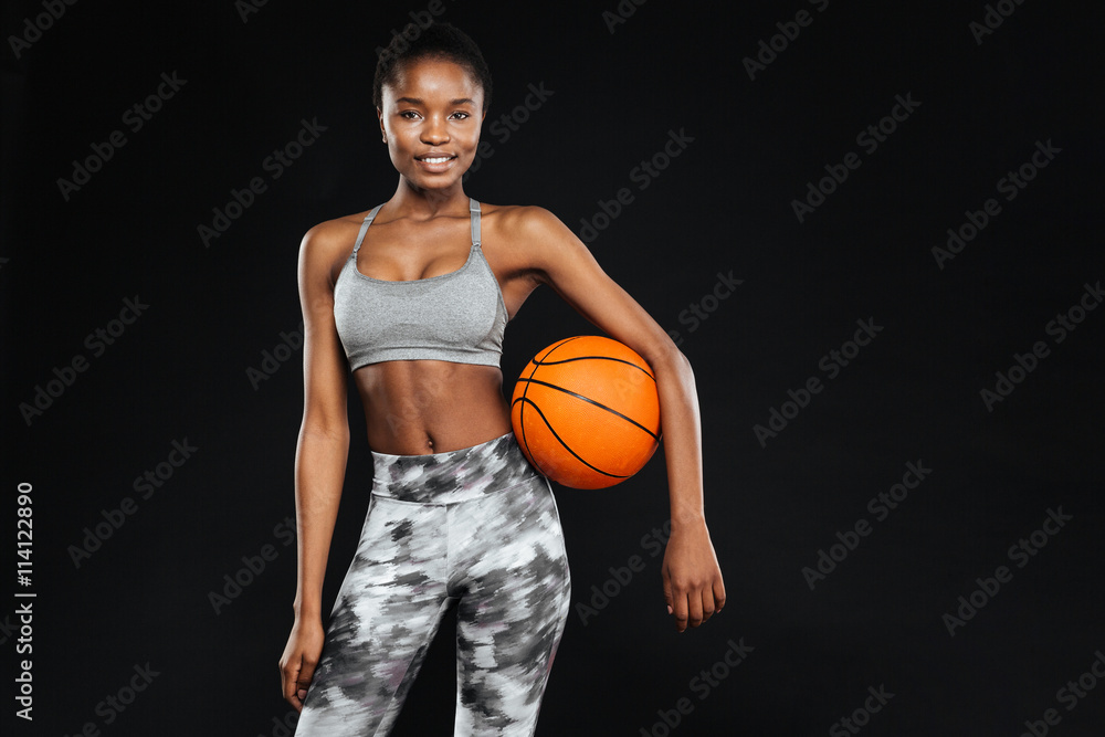 Happy beautiful sports woman holding ball over black background