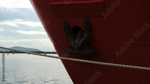 Bow of red metal ship with rusty anchor moored at harbor dock.