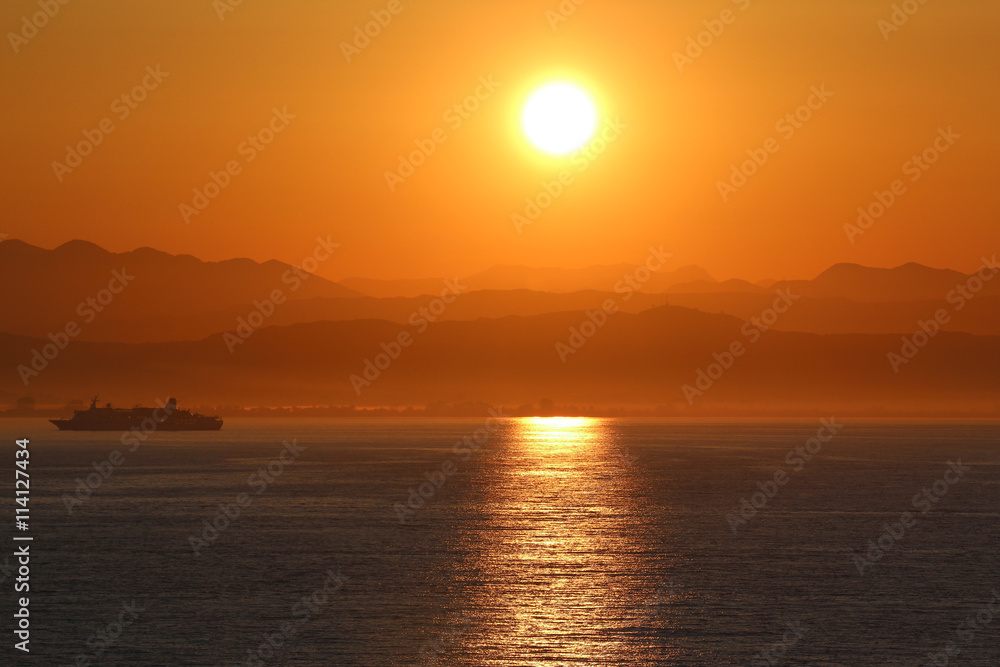 Sonnenaufgang an Küste mit Berglandschaft und Schiff