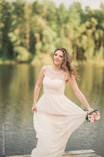 Gorgeous bride in elegant dress holding bouquet posing near forest and lake © olegparylyak