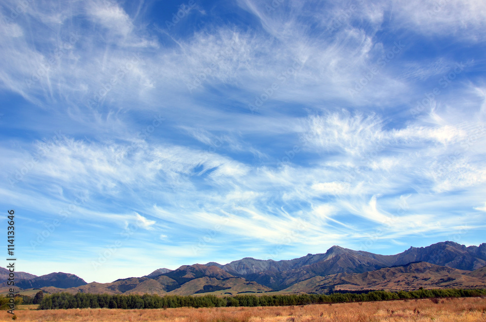 Wispy clouds in blue skies above a rugged mountain range in New Zealand