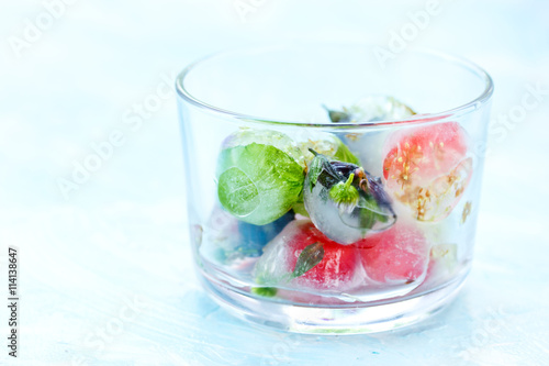 Fresh fruits and berry frozen in ice cubes on blue background
