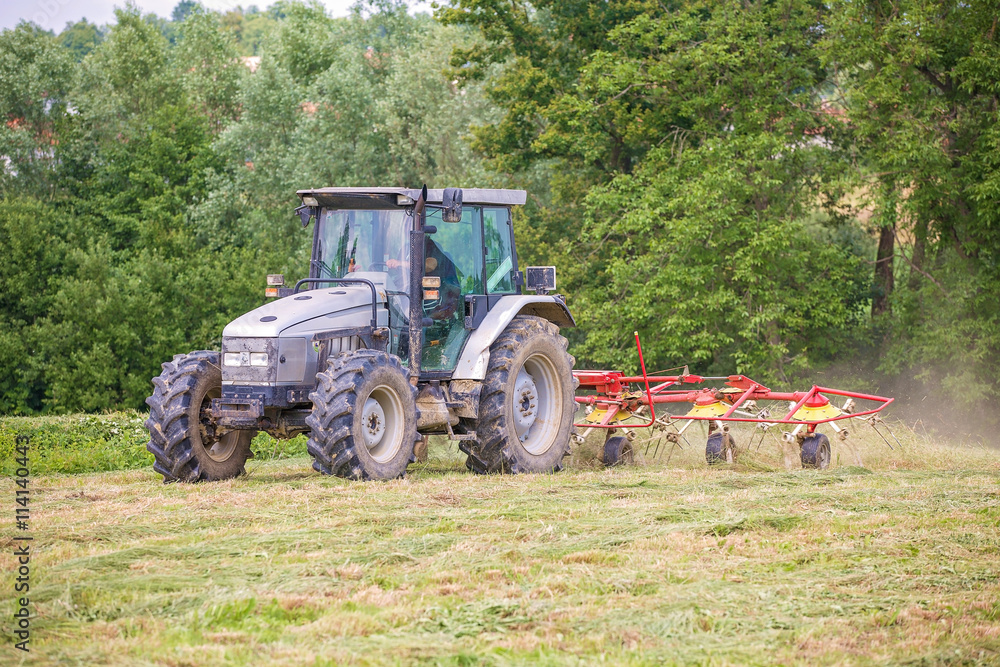 Farmer driving a tractor on the field with the attached tool used to spread hay on the field Farmer driving a tractor on the field with the attached tool used to spread hay on the field
