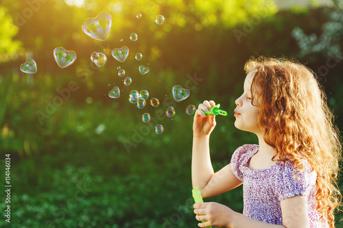 Little girl blowing soap bubbles, happy childhood concept.