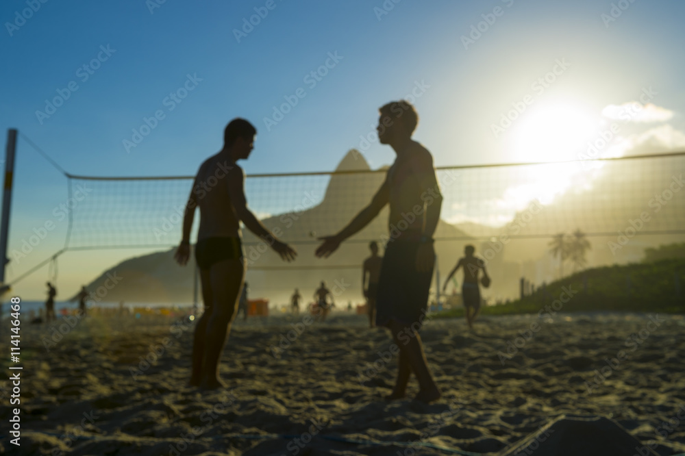Fototapeta premium Defocus view of silhouettes of Brazilians shaking hands on a beach volleyball court in Rio de Janeiro, Brazil at sunset on Ipanema Beach
