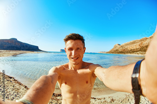 man is sunbathing on the sand on the beach. Male partially in water  taking selfie