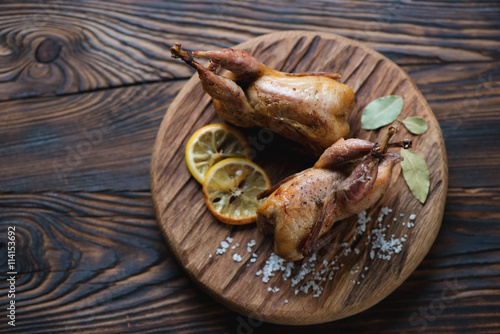 Serving board with whole baked quails in a rustic wooden setting