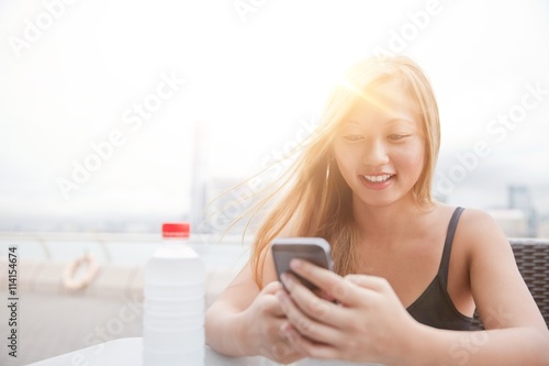 Young woman sitting beside harbour, using smartphone, Hong Kong, China photo