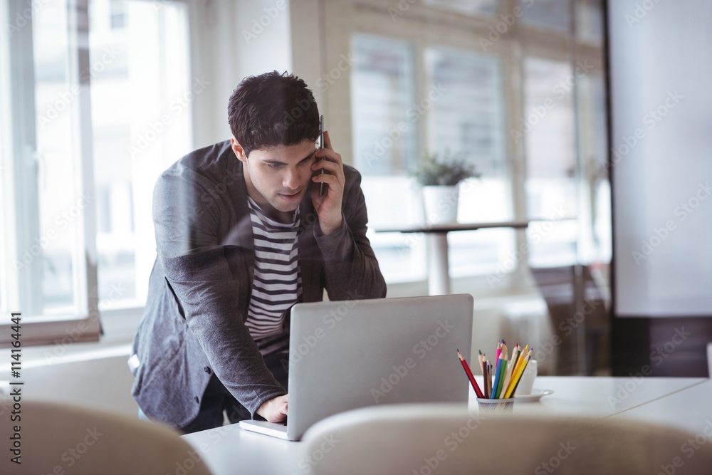 Businessman talking on smartphone while working on laptop in office Businessman talking on smartphone while working on laptop in office