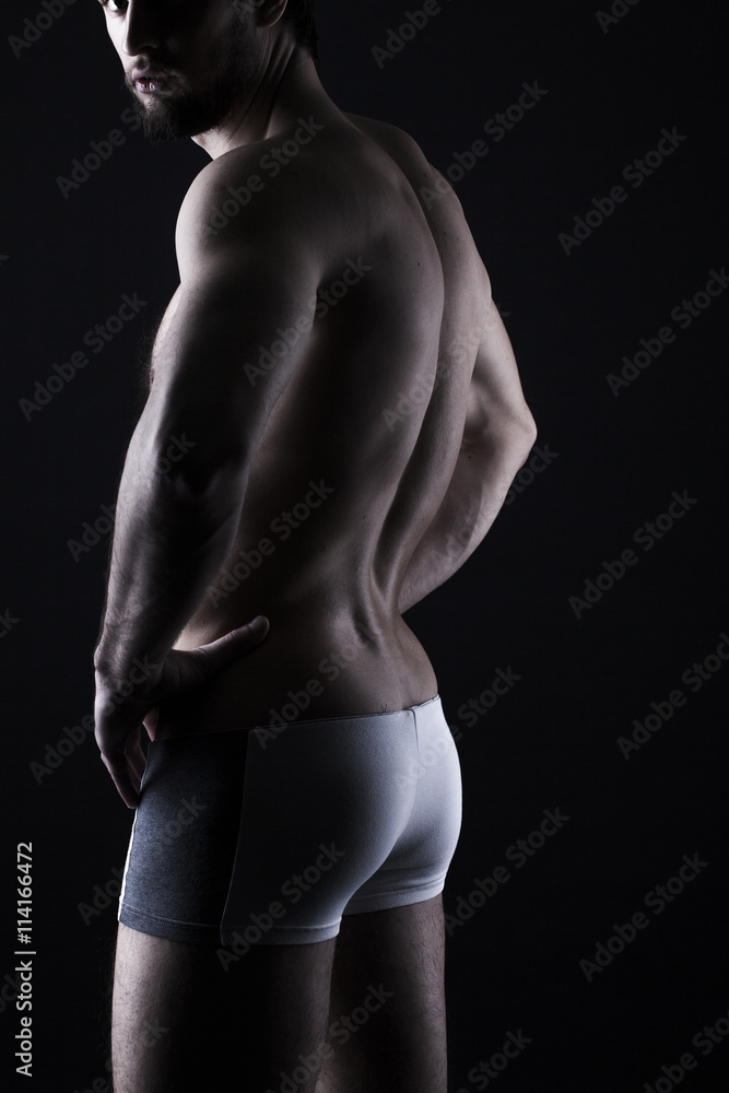 Fototapeta premium beautiful men's sporty body in backlight on the black background