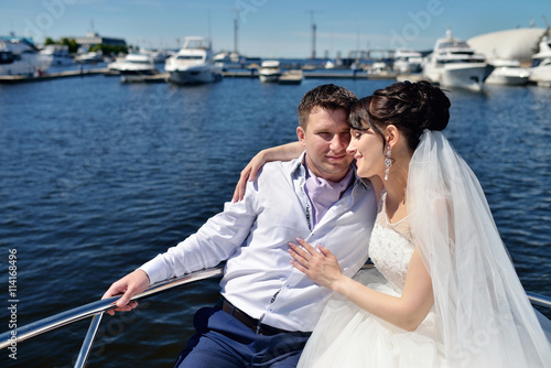 Wedding couple is hugging on a yacht. Beauty bride with groom. Beautiful model girl in white dress. Man in suit. Female and male portrait. Woman with lace veil. Cute lady and guy outdoors © pvstory