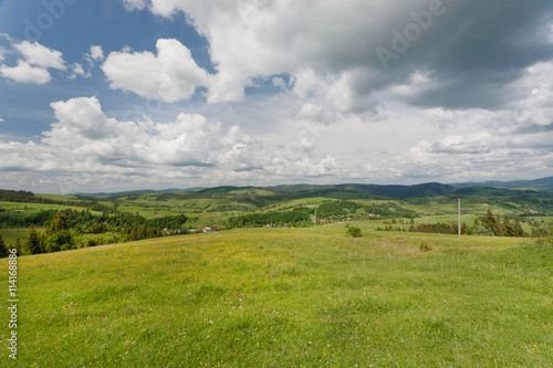 Dramatic sky with clouds over green hills of small village in Carpathian mountains.