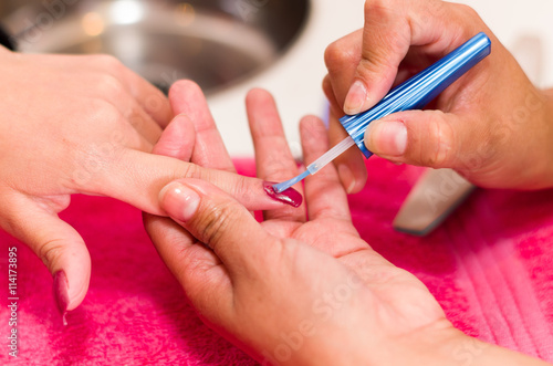 Closeup females hands getting manicure treatment from woman using small brush in salon environment  pink towel surface  blurry background products