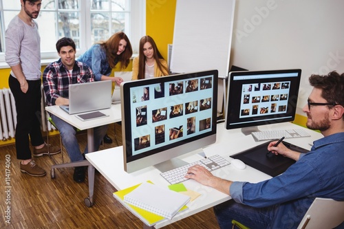 Photo editor working on computer against coworkers