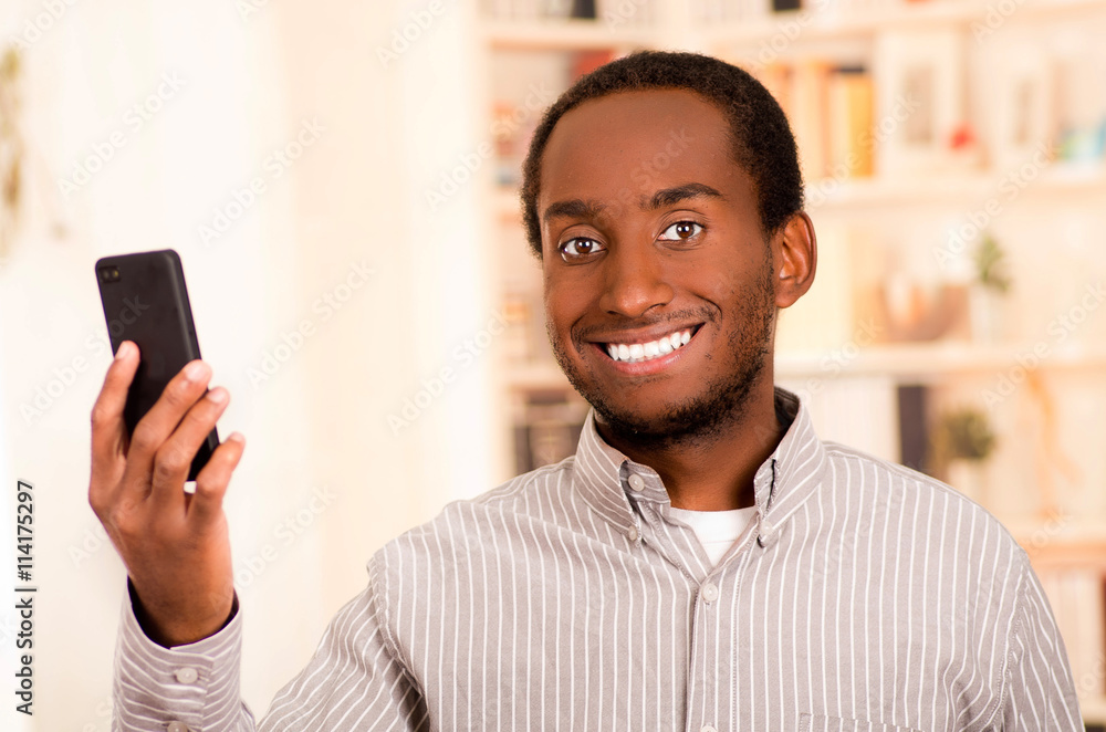 Handsome man wearing casual clothes holding up mobile phone looking into camera and smiling Handsome man wearing casual clothes holding up mobile phone looking into camera and smiling