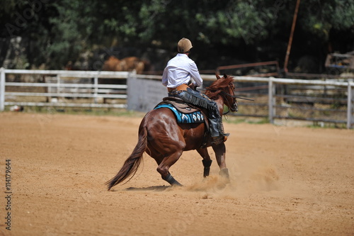 A rear view of a rider on horseback sliding in the dust.