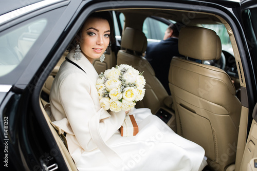 Wedding Day: beautiful bride with bouquet of white flowers in the car