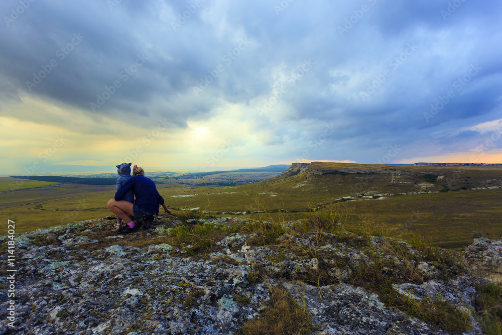 Fototapeta premium Mom shows her daughter the view of the valley from a high mountain