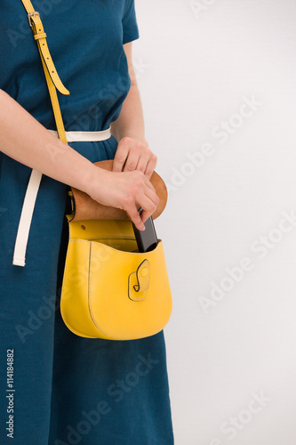 Closeup of woman's hands taking out smartphone from yellow purse. Image of young stylish woman taking cellphone out of handbag. Girl with phone. Communication and lifestyle concept