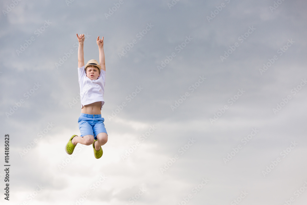 Cute kid boy jumping into cloudy sky - happiness, childhood, freedom, lifestyle concept - smiling boy in straw hat jumping in air over grey rainy sky. Cute kid boy jumping into cloudy sky - happiness, childhood, freedom, lifestyle concept - smiling boy in straw hat jumping in air over grey rainy sky.