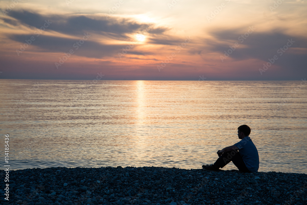 Man silhouette sitting on beach with sea and sunset background