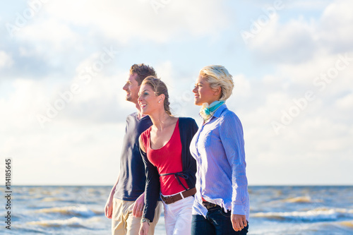 Freunde, Frauen und Mann, spazieren durch Sand und Wellen am Nordsee Strand 