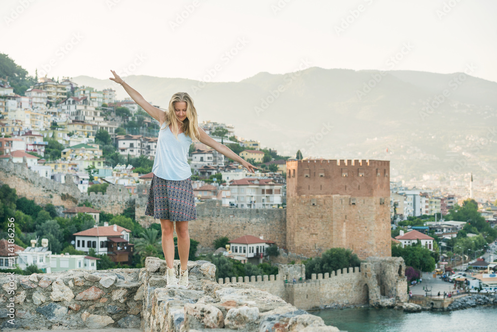 Young blond woman tourist balancing on ancient fortress wall of Alanya castle.