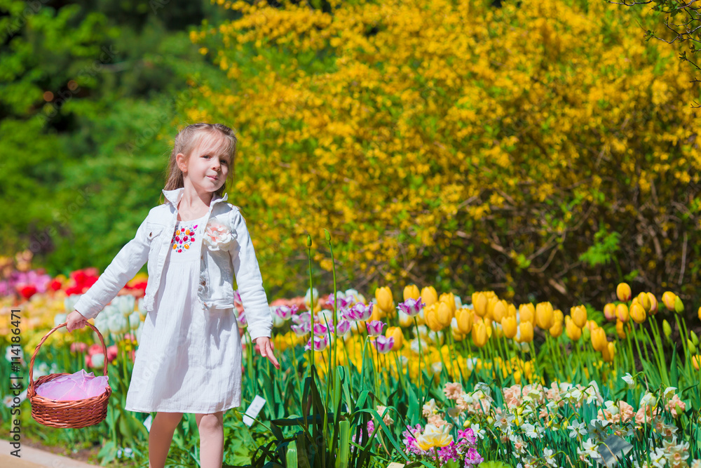 Spring garden, spring flowers, adorable little girl and tulips. Cute kid with a basket in blooming garden on warm day Spring garden, spring flowers, adorable little girl and tulips. Cute kid with a basket in blooming garden on warm day