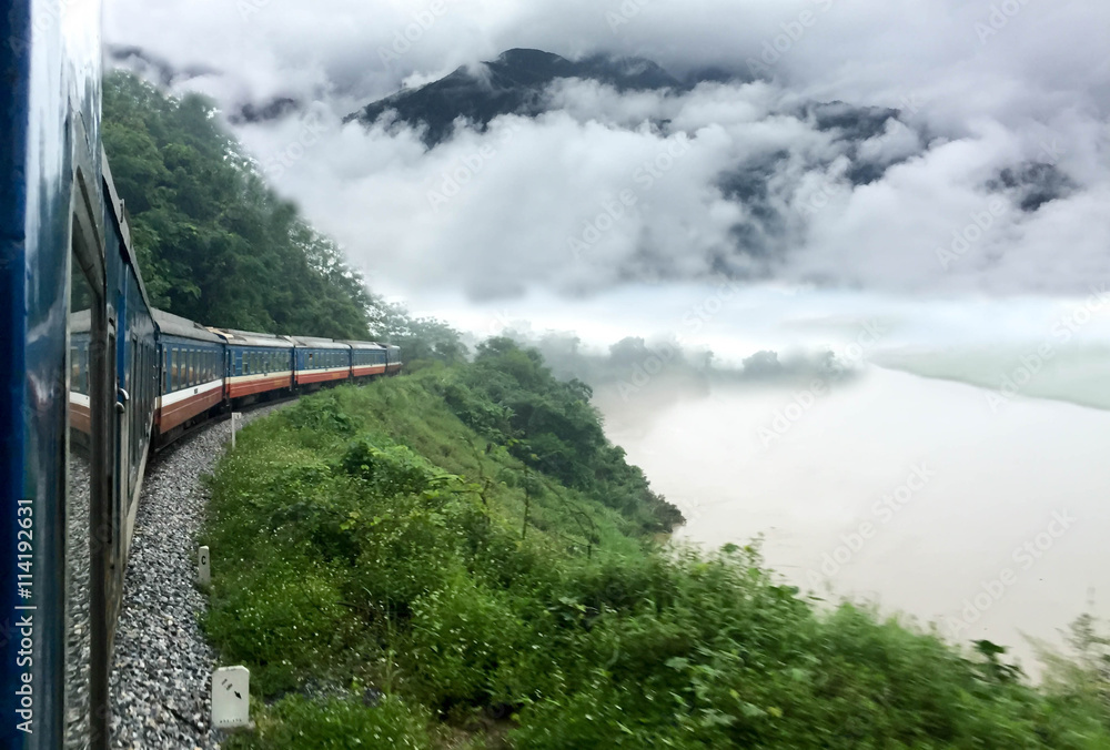 Fototapeta premium Train passing a beautiful fog mountains and river