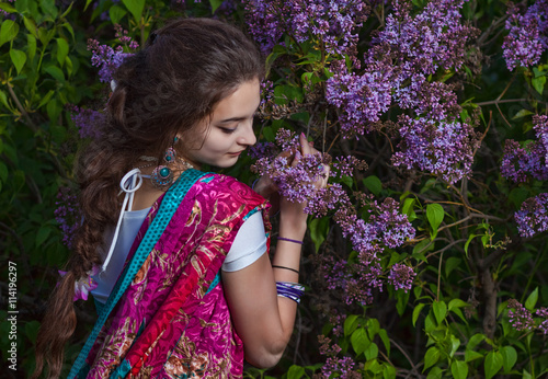 Asian woman dressed in sari in lilac bushes at sunset