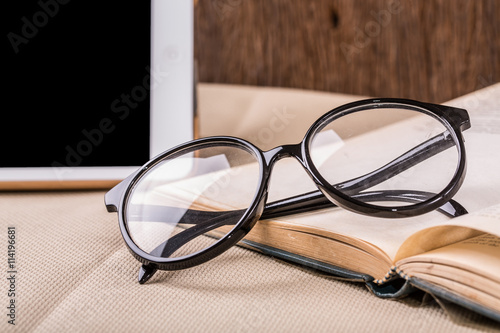 Reading table with tablet PC and old book and eyeglasses