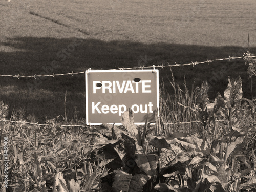 Sepia private keep out sign on barbed wire boundary fence to farmland photo