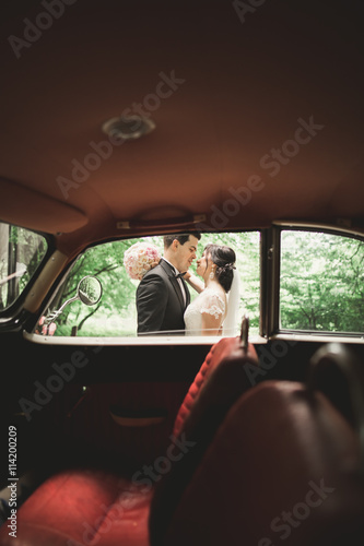 Beautiful wedding couple posing near splendid retro car © olegparylyak