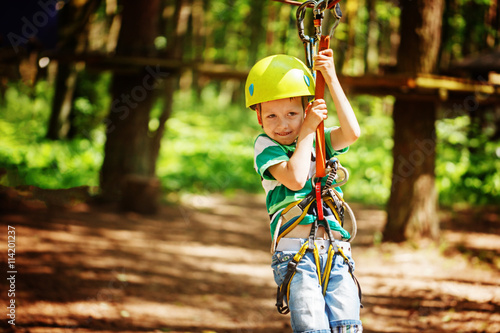 Adventure climbing high wire park - little child on course in mountain helmet and safety equipment
