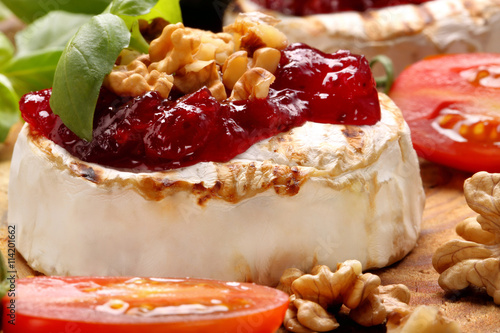 Grilled brie cheese with cranberry jam and walnuts on old wooden