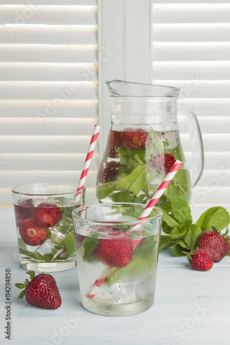 Summer cold drink with strawberry, mint and ice on a light backg