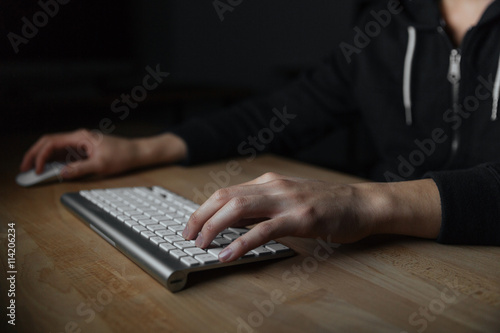 Hands of young man typing on keyboard in dark room