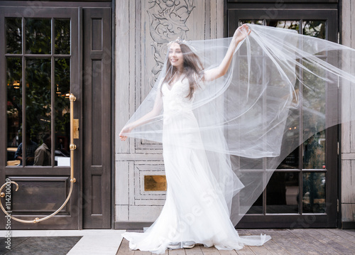 Happy bride covered with flying veil standing on street