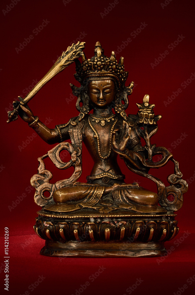 Statuette of Manjushri on a red background.