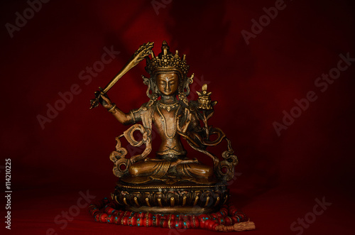 Statuette of Manjushri on a red background.