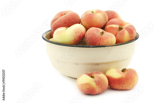 fresh colorful flat peaches (donut peaches) in an enamel bowl on a white background