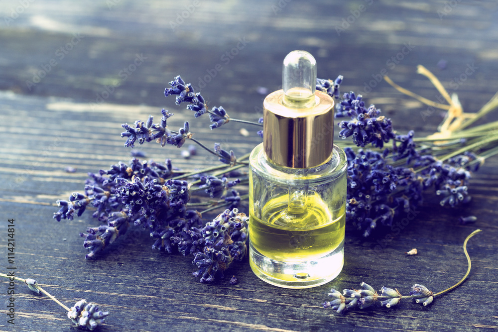 Obraz premium Bottle of lavender oil and lavender flowers on wooden background - vintage stylized photo